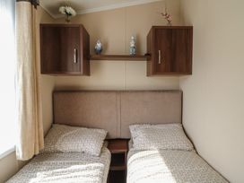 A bedroom with two single beds side by side under two wooden wall cabinets and a wooden shelf at Heulwen in New Quay