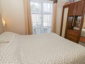 A bedroom with a double bed and patterned bedding next to a window with curtains and a wooden wardrobe with mirror and drawers at Heulwen in New Quay