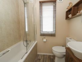 A bathroom with a bathtub shower combination a toilet a sink with wooden cabinet and a window with blinds at Heulwen in New Quay