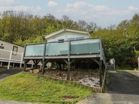 A raised mobile home with frosted glass railing and wooden supports surrounded by trees at Heulwen in New Quay