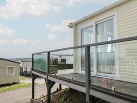 A balcony with glass railing attached to a beige mobile home with a road and other mobile homes in the background at Heulwen in New Quay