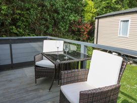 A patio with two wicker chairs with white cushions and a glass table with two wine glasses near a mobile home in a garden at Heulwen in New Quay