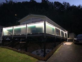 A raised home with illuminated frosted glass balcony panels and a driveway with a parked car at Heulwen in New Quay