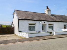 A white single-story cottage with a tiled roof and small front wall along a street at Cobweb Cottage in Waunfawr
