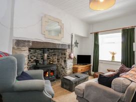 A living room with a wood stove fireplace armchairs a sofa a coffee table and a television at Cobweb Cottage in Waunfawr