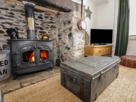 A stone fireplace with a wood-burning stove and a metal chest coffee table in front a wooden TV stand with a television and a brown leather pouf in a living room at Cobweb Cottage in Waunfawr