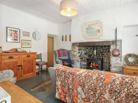 A living room with a wood stove fireplace an armchair a wooden cupboard a patterned sofa and framed pictures on the wall at Cobweb Cottage in Waunfawr