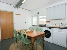 A kitchen with a wooden table and four green chairs a washing machine and dishwasher under the counter at Cobweb Cottage in Waunfawr