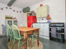 A kitchen with a wooden dining table and green chairs a red refrigerator a black oven and white cabinets at Cobweb Cottage in Waunfawr