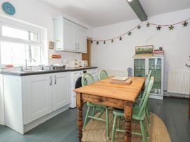 A kitchen with a wooden dining table and green chairs next to a sink and cabinets at Cobweb Cottage in Waunfawr