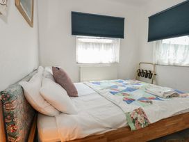 A bedroom with a bed covered with white sheets and a multicolored quilt under two windows with blue blinds at Cobweb Cottage in Waunfawr