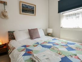 A bedroom with a bed with patterned quilt and pillows a bedside table with a lamp and a window with a blue blind at Cobweb Cottage in Waunfawr