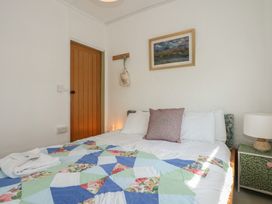 A bedroom with a bed covered with a colorful quilt a pillow towels on the bed a bedside table with a lamp a wooden door a painting on the wall at Cobweb Cottage in Waunfawr