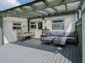 A covered outdoor patio with a gray sectional sofa a glass coffee table a hanging bench and a wooden shelf at Cobweb Cottage in Waunfawr
