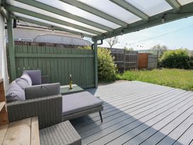 An outdoor covered deck with patio furniture and a bottle on a glass table at Cobweb Cottage in Waunfawr