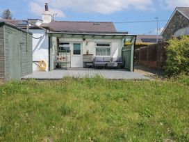 A backyard with grass lawn a wooden deck outdoor seating and shed at Cobweb Cottage in Waunfawr