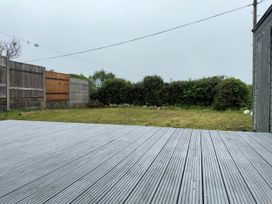 A garden with grass and a wooden deck area at Cobweb Cottage in Waunfawr