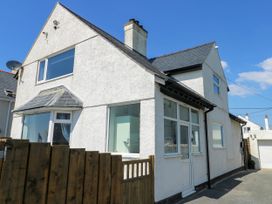 A white two-story house with multiple windows a small wooden fence and gate at Annedd Wen in Rhosneigr