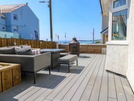 An outdoor patio with grey seating, a fire pit, and a wooden fence overlooking the sea at Annedd Wen in Rhosneigr