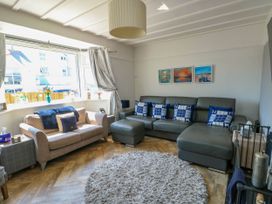 A living room with a beige sofa a gray sectional sofa with blue pillows a round gray rug and paintings on the wall at Annedd Wen in Rhosneigr