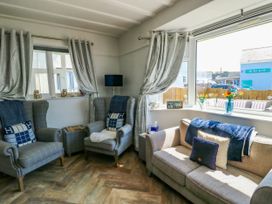 A sitting room with two armchairs and a sofa near windows with curtains and flowers on the windowsill at Annedd Wen in Rhosneigr