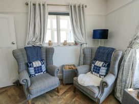 A sitting area with two checkered armchairs a small table and a window with curtains at Annedd Wen in Rhosneigr