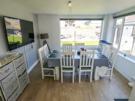 A dining room with a table and chairs next to large windows showing a garden outside at Annedd Wen in Rhosneigr