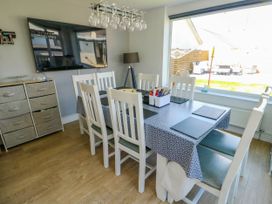 A dining room with a table covered with a patterned tablecloth and six chairs at Annedd Wen in Rhosneigr