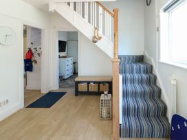 An entryway with a staircase covered in striped carpet a bench with baskets and a lantern on the floor at Annedd Wen in Rhosneigr