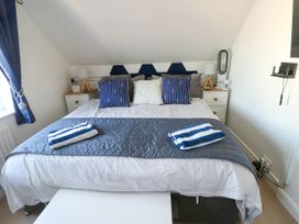 A bedroom with a double bed blue striped pillows and towels bedside tables lamps and a window with blue curtains at Annedd Wen in Rhosneigr