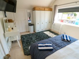 A bedroom with a bed, a gray rug, white wardrobe, dressing table, and large window at Annedd Wen in Rhosneigr