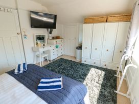 A bedroom with a bed with striped towels a white wardrobe a white dresser a wall-mounted TV and a blue rug at Annedd Wen in Rhosneigr