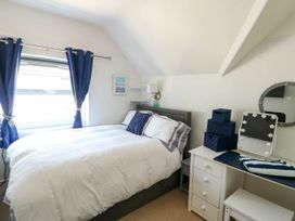 A bedroom with a bed a window with curtains a dresser with storage baskets and a mirror at Annedd Wen in Rhosneigr