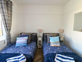 A bedroom with two single beds blue bedding pillows bedside tables lamps and a window with plaid curtains at Annedd Wen in Rhosneigr