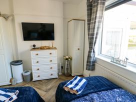 A bedroom with a wall mounted TV a white chest of drawers a small cabinet and a window with curtains at Annedd Wen in Rhosneigr