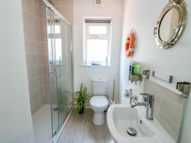 A bathroom with a shower enclosure a toilet a sink a plant and a round mirror at Annedd Wen in Rhosneigr