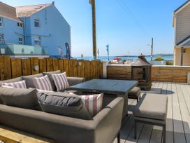 An outdoor seating area with gray sofas and striped cushions beside a fire pit and wooden fence at Annedd Wen in Rhosneigr