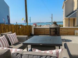 An outdoor patio with gray sofas and striped cushions around a black table and a fire pit overlooking the sea at Annedd Wen in Rhosneigr