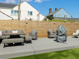 An outdoor patio with gray seating furniture a table and a covered barbecue grill at Annedd Wen in Rhosneigr
