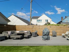 An outdoor seating area with chairs a table and a covered object on a deck behind a wooden fence at Annedd Wen in Rhosneigr