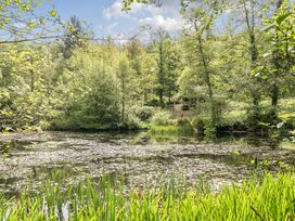 A peaceful pond surrounded by trees with a wooden house at Harcombe House Bungalow – Pet Friendly with Wet Room in Chudleigh