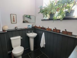 A bathroom with a white toilet and pedestal sink a wall mirror framed artwork plants on the windowsill and decorative wooden items on a ledge at Zoar Chapel in Carew