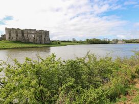 Ruins of a stone castle beside a river with green bushes in the foreground and houses in the background at Zoar Chapel in Carew