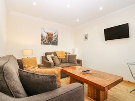 A living room with brown sofas a wooden coffee table a wall-mounted television and artwork at Smiddy Bothy in Edzell
