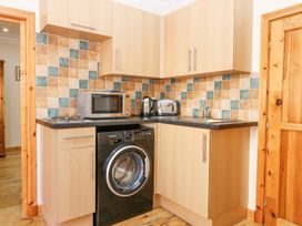 A kitchen corner with wooden cabinets a washing machine microwave kettle toaster and a sink at Smiddy Bothy in Edzell