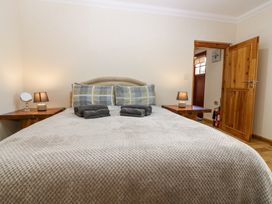A bedroom with a bed covered with a textured blanket and folded towels two wooden bedside tables with lamps and a door open at Smiddy Bothy in Edzell