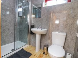 A bathroom with a glass shower enclosure a pedestal sink a toilet a trash can and a bath mat on a wooden floor at Smiddy Bothy Edzell