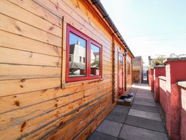 A walkway beside a wooden building with red windows and door at Smiddy Bothy in Edzell