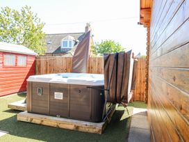 An outdoor area with a wooden hot tub on artificial grass next to a red shed and a wooden fence at Smiddy Bothy in Edzell