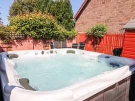 An outdoor hot tub with bubbling water near a red fence and garden chairs at Smiddy Bothy in Edzell